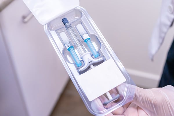 Doctor holding package of dermal filler with syringe vial and needles